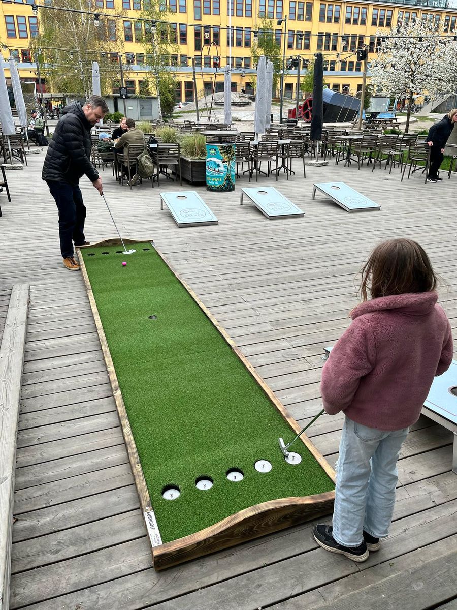 Man och flicka spelar Kubbgolf på en takterrass, med Corn Hole synligt i bakgrunden
