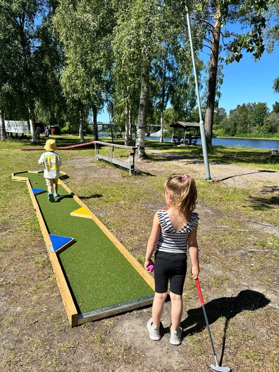 Barn som spelar minigolf bland björkar vid vattnet